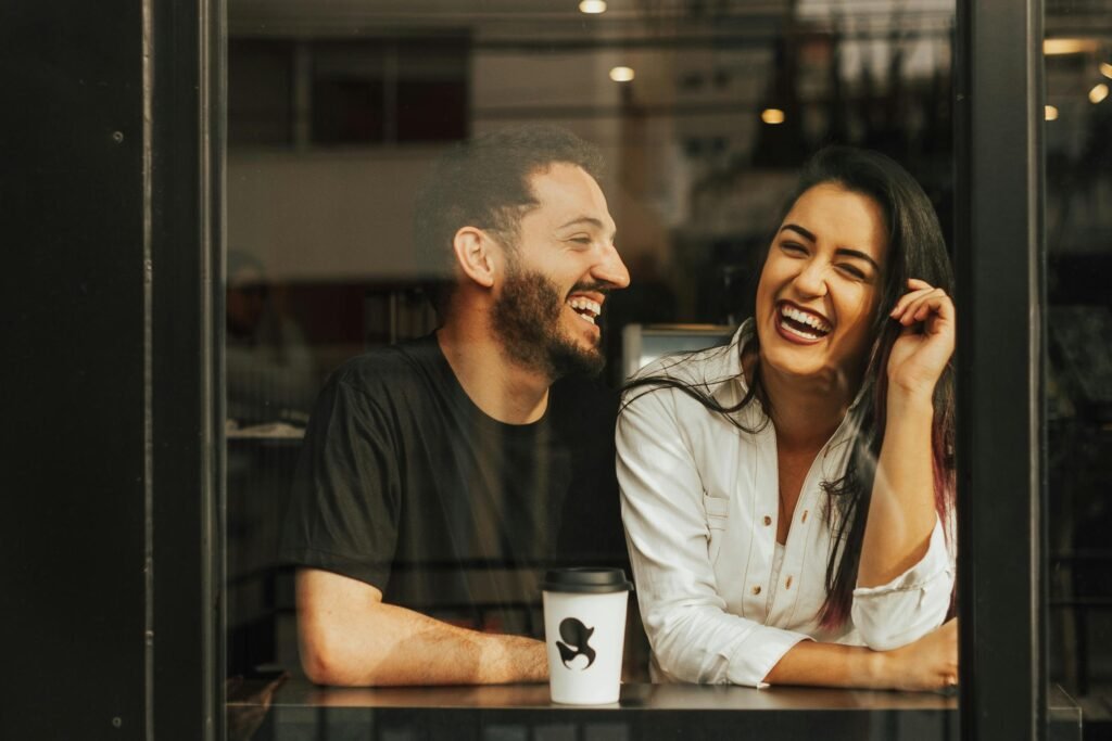 pexels-photo-16756653-16756653 A man and woman laughing together at a café window with coffee.